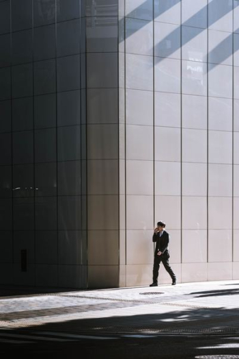 person walking beside gray building person walking beside gray building