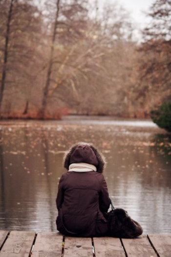 person wearing parka jacket sitting on wooden dock person wearing parka jacket sitting on wooden dock