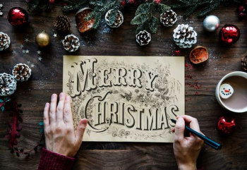 person writing Merry Christmas on paper in between Christmas decors