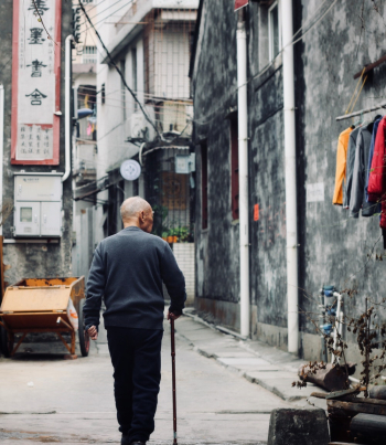Photo of an elderly man walking on an alley Photo of an elderly man walking on an alley