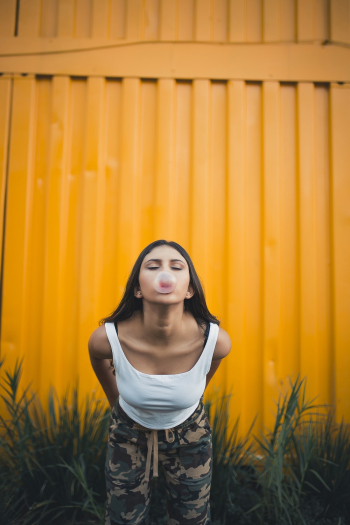 Photo of Woman Blowing Bubble Gum While Leaning Over Near Yellow Intermodal Container