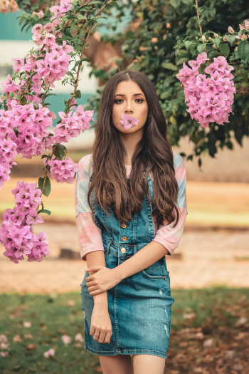 Photo of Woman with Pink Flower in Her Mouth Posing Next to Bougainvillea Plant 