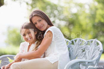 Portrait affectionate mother hugging daughter on bench in garden Portrait affectionate mother hugging daughter on bench in garden