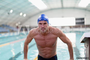 Portrait confident athletic male swimmer at edge of swimming pool