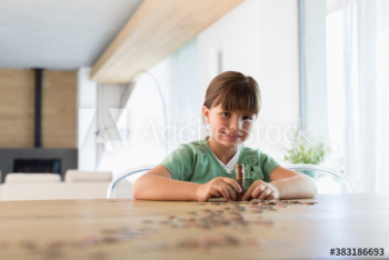Portrait confident girl counting and stacking coins at dining table Portrait confident girl counting and stacking coins at dining table