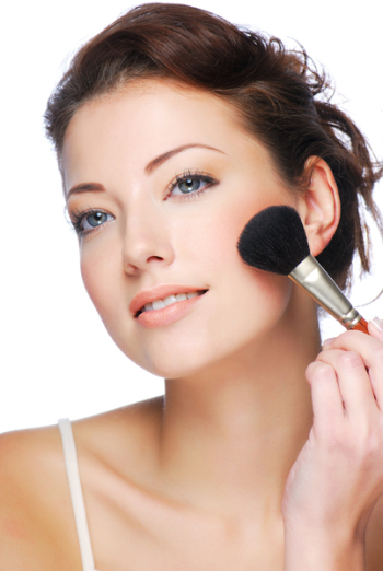 Portrait of attractive young adult woman applying blusher