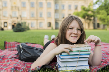 Portrait of school girl laying on blanket with books Free Photo