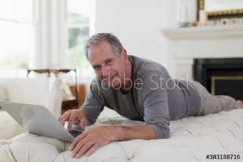 Portrait smiling senior man using laptop on ottoman Portrait smiling senior man using laptop on ottoman