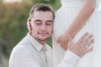 Pregnancy, man is listening to the baby inside woman's belly with closed eyes outdoors Free Photo