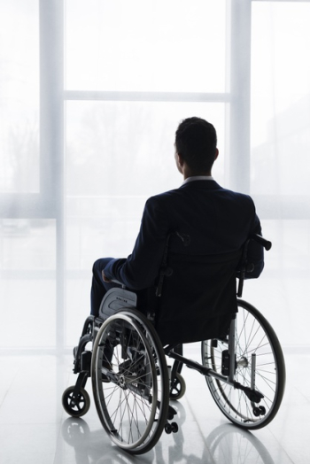 Rear view of a businessman in suit sitting on wheelchair looking at window Free Photo