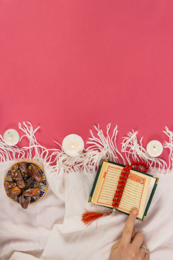 Red rosary; lighting candle; holy book of koran and dates in bowl on shawl over red background