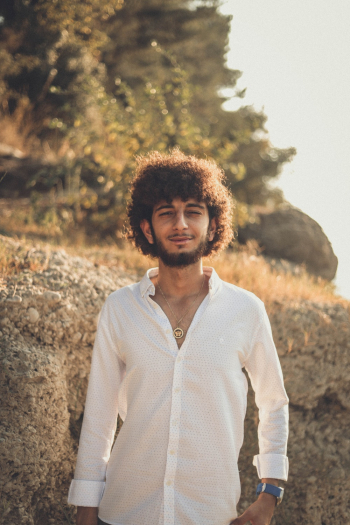 Selective Focus Photo of Man in White Dress Shirt Standing Alone In Front of Rock