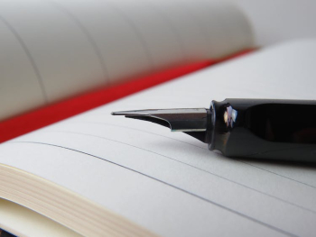 Selective Focus Photography of Calligraphy Pen Placed on Top of Open Notebook