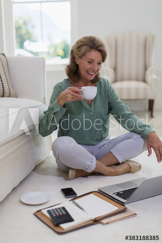 Senior woman drinking coffee at laptop on living room floor Senior woman drinking coffee at laptop on living room floor