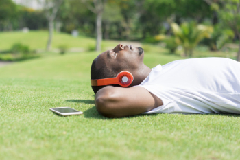 Serene black man resting in park and listening to music. Serene black man resting in park and listening to music.