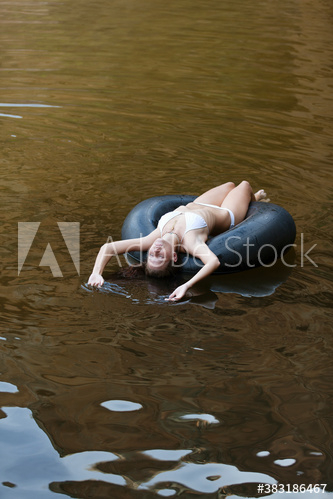 Serene young woman in bikini floating on inner tube on lake Serene young woman in bikini floating on inner tube on lake