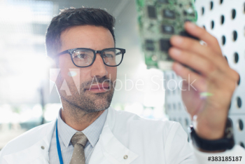 Serious male engineer examining circuit board Serious male engineer examining circuit board