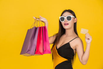 Shopping  beautiful woman wearing glasses with a gold credit card with a colorful paper bag on a yellow  . Free Photo