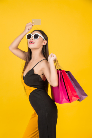 Shopping  beautiful woman wearing glasses with a gold credit card with a colorful paper bag on a yellow  . Free Photo