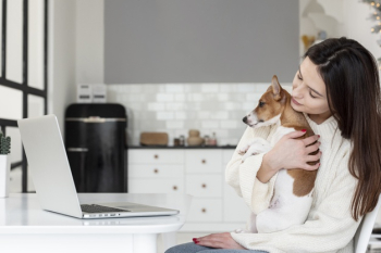 Side view of woman holding her dog while looking at laptop Free Photo