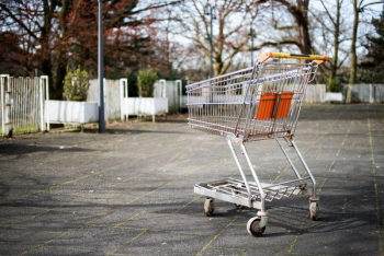 silver metal shopping cart on gray pavement near white fences