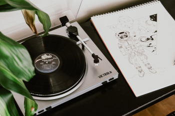 Silver sophisticated Victrola record player on a desk next to a beautiful hand drawing of an astronaut. 