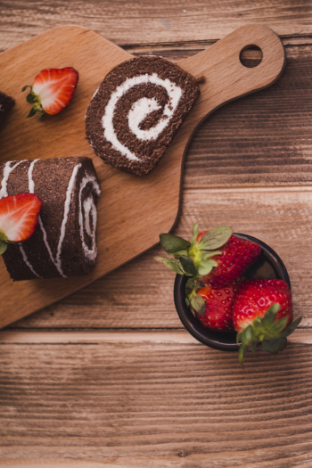 Slices of tasty roll and strawberries on wooden table Slices of tasty roll and strawberries on wooden table