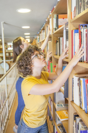 Smart teenager looking for book near friend Smart teenager looking for book near friend
