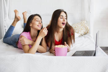 Smiley women watching at laptop and eating popcorn Free Photo