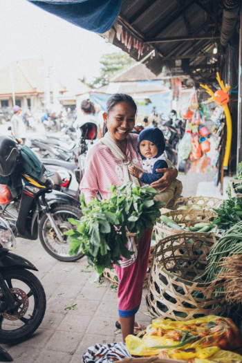Smiling Woman Carrying Baby and Holding Green Leafy Vegetable Smiling Woman Carrying Baby and Holding Green Leafy Vegetable