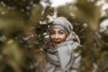 Smiling Woman Wearing Grey Coat and Cap Beside Green Plants Smiling Woman Wearing Grey Coat and Cap Beside Green Plants