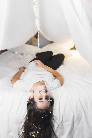Smiling young woman relaxing bed with ferry light on her hair