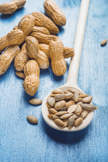 Sunflower seeds in wooden spoon with raw whole peanuts on blue painter backdrop