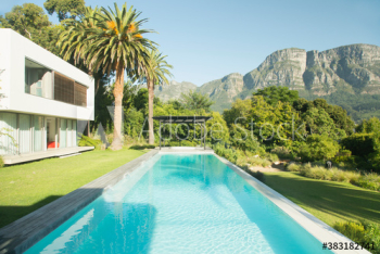 Sunny tranquil swimming pool outside luxury house below mountain Sunny tranquil swimming pool outside luxury house below mountain
