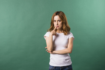 Thoughtful young woman with her finger on lips against green backdrop