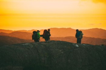 three hikers standing on cliff during golden time