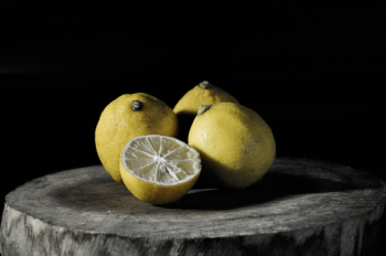 Three Lemons Beside Sliced Lemon on Tree Slab Three Lemons Beside Sliced Lemon on Tree Slab