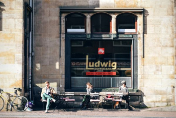 Three People Sitting on Bench in Front of Ludwig Coffee Bar