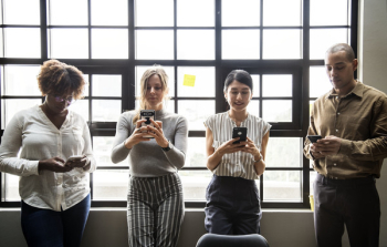 Three Women and One Man Standing While Using Phones Three Women and One Man Standing While Using Phones