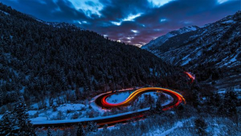 timelapse photography of curved road between mountain with trees timelapse photography of curved road between mountain with trees