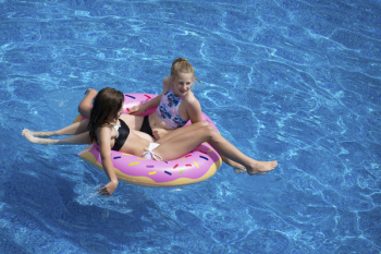 Two Girls Sitting on Pink Doughnut Pool Float Two Girls Sitting on Pink Doughnut Pool Float