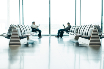Two Men Sitting in Front of Each Other on White Gang Chairs in Airport Waiting Area