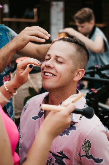 two people putting makeup on man's face