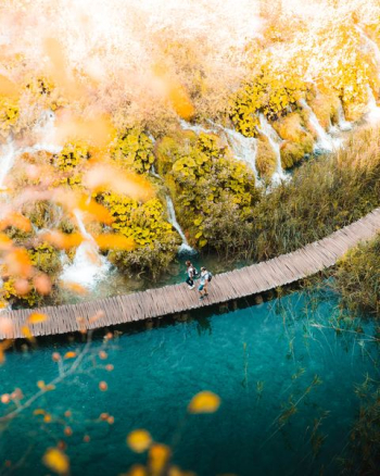 two person walking on boardwalk over body of water two person walking on boardwalk over body of water