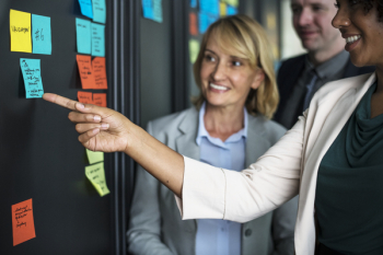 Two Women and Man Standing in Front of Wall Board