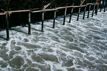 Water Flowing Underneath The Shadowy Pier Water Flowing Underneath The Shadowy Pier