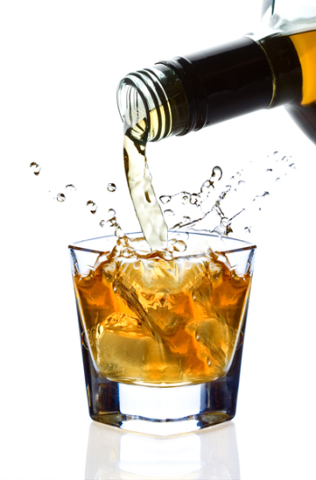 Whiskey being poured into a glass against white background