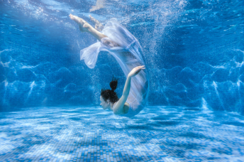 Woman dances under the water, she is in the pool.
