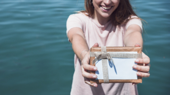 Woman holding gift in front of sea water background Woman holding gift in front of sea water background