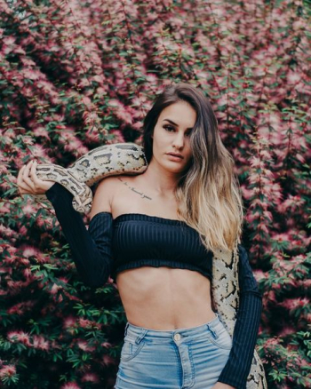 woman holding python snake near pink petaled flowers woman holding python snake near pink petaled flowers
